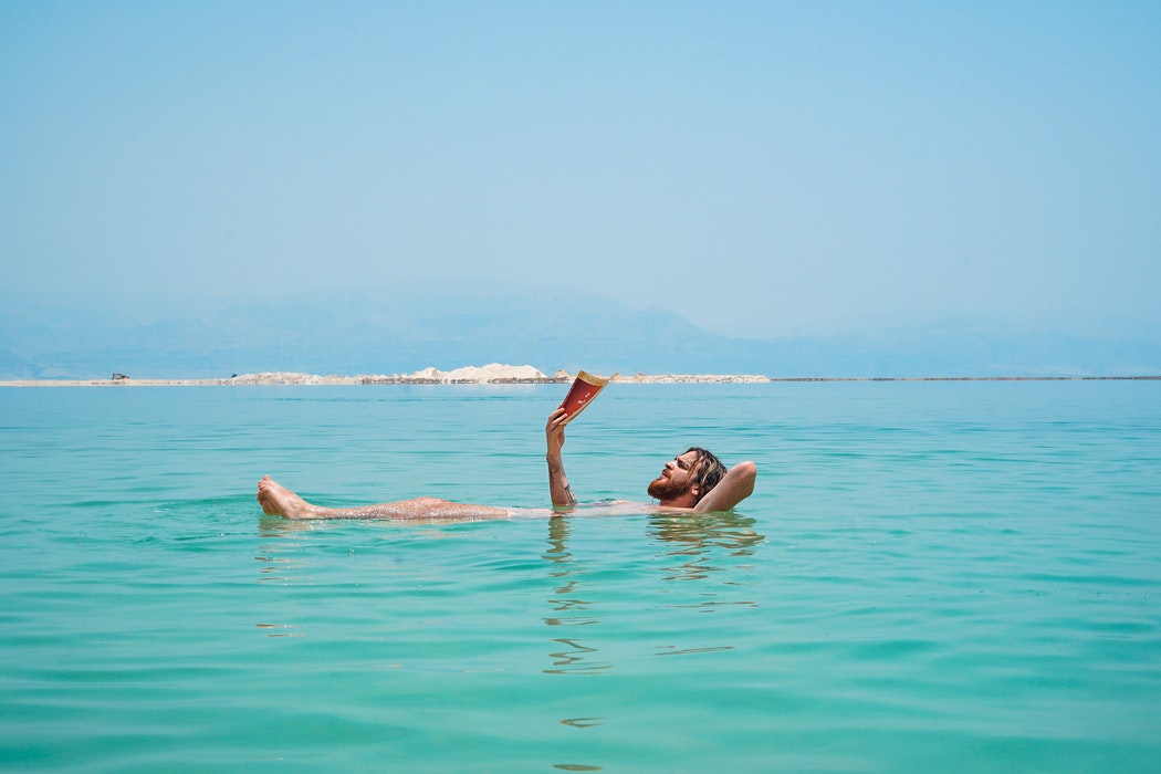 Man reading a book in water: 6 Best Summer Beach Reads to Take on Your Next Vacation